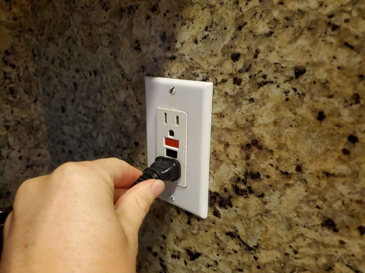 hand of a man plugging an electrical cord into a Ground Fault Circuit Interrupter (GFCI) electrical outlet on the wall