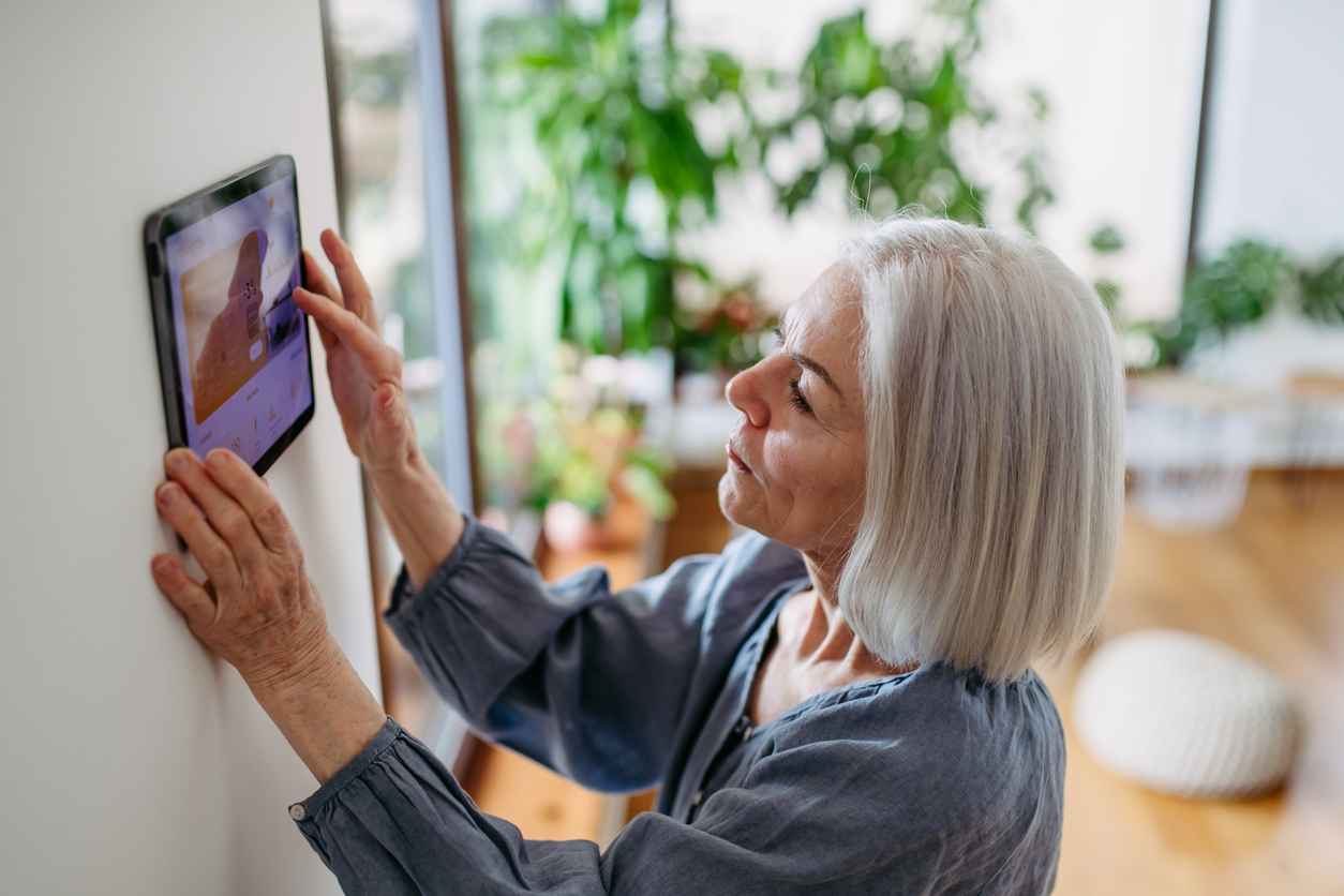 Older woman using smart technology at her home and adjusting a smart thermostat.